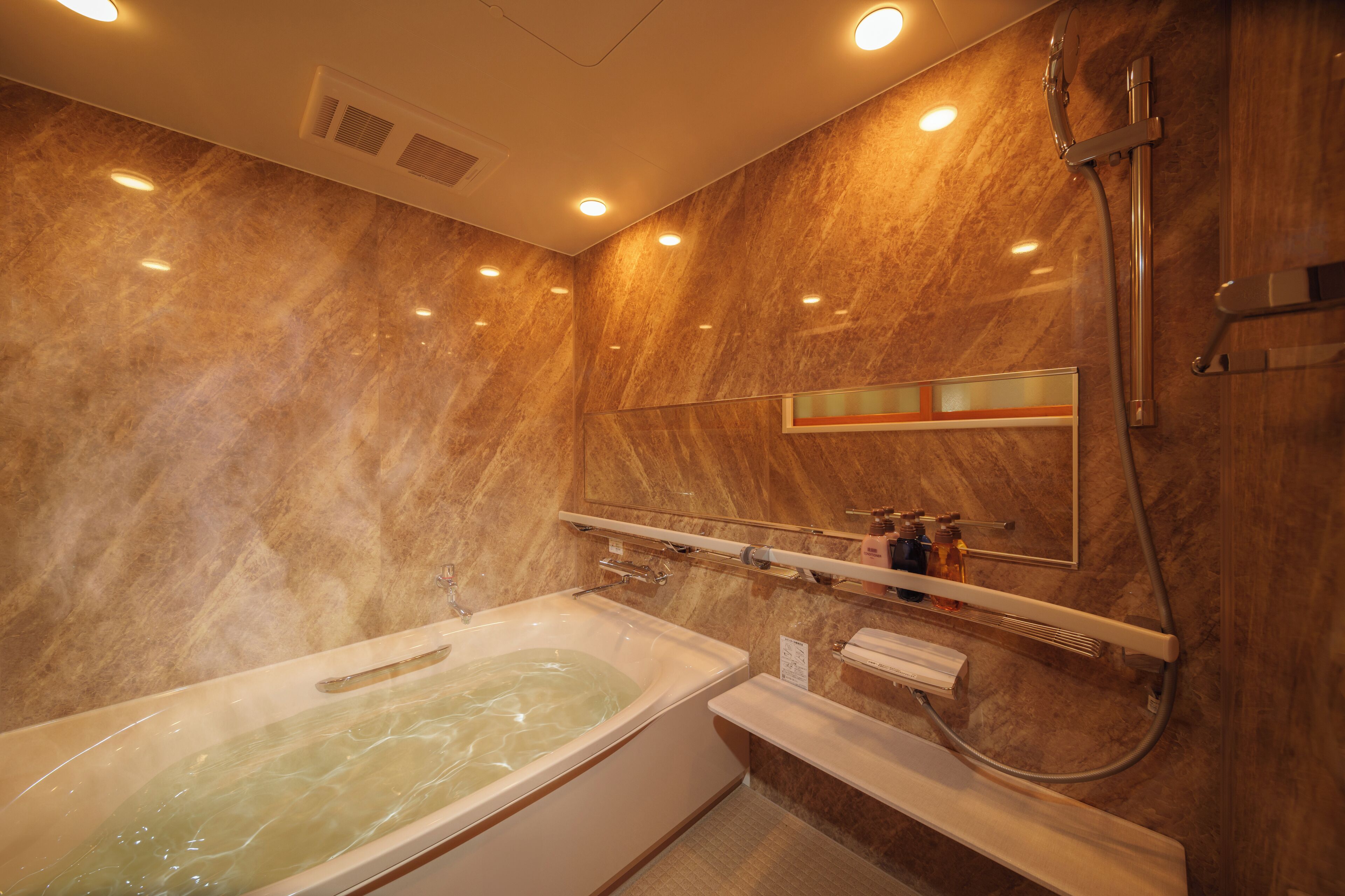 A bathroom with a marble wall, a bathtub, a shower, and a mirror.
