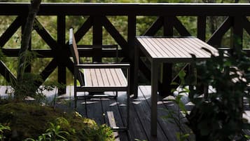 A wooden deck with a bench and a table, surrounded by greenery.