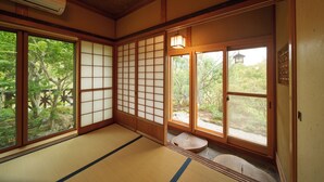 Une pièce de style japonais traditionnel, avec un sol recouvert de tatamis, des portes coulissantes et une vue sur la verdure environnante.