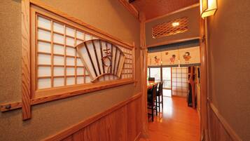 A traditional Japanese interior with wooden sliding doors, a dining area with chairs, and a view of a garden through a window.