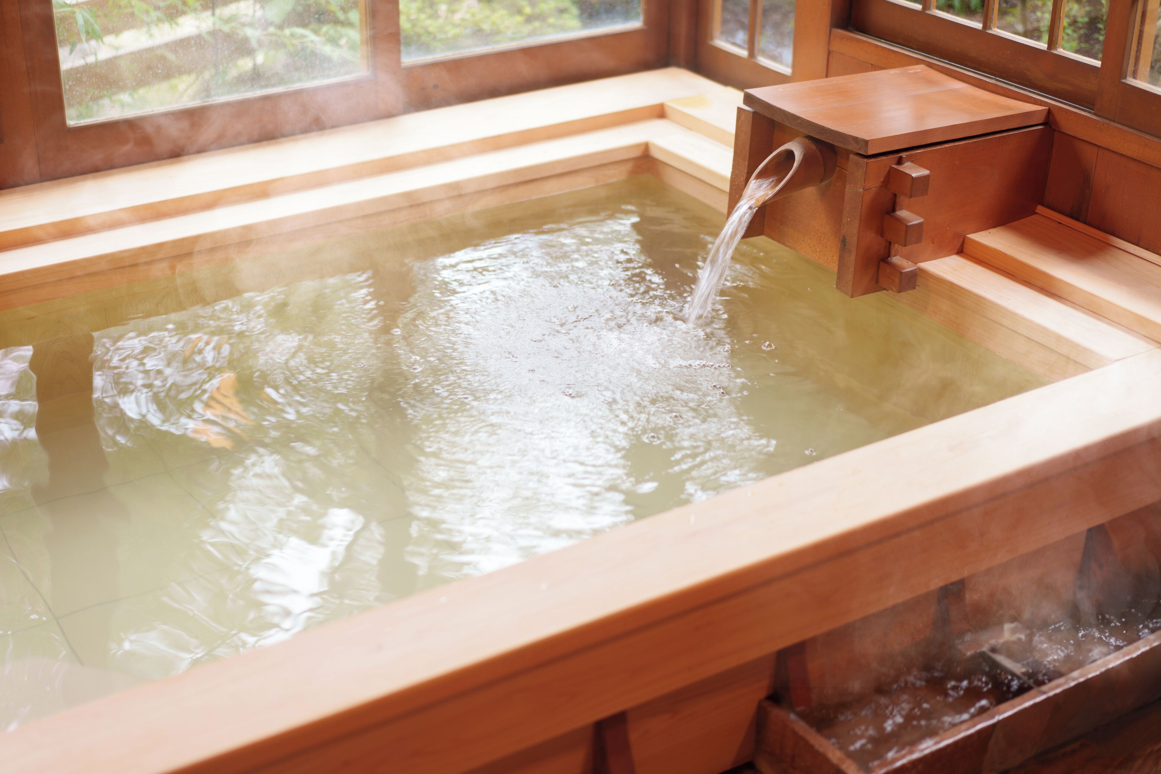 A wooden hot spring bath with a wooden bench and steps leading into the water.