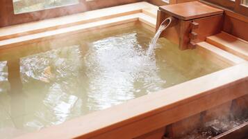 A wooden hot spring bath with a wooden bench and steps leading into the water.