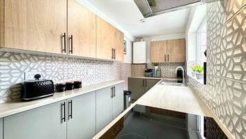 Une cuisine moderne avec des meubles en bois, une plaque de cuisson à induction noire et un crédence décorée.