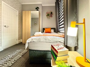 A bedroom with a bed, bedside table, lamp, and a stack of books.