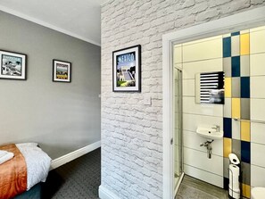 Une chambre d’hôtel avec un lit, un mur d’accent en briques blanches, une salle de bain avec un lavabo et des toilettes, et des tableaux encadrés accrochés au mur.
