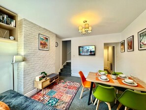 Un coin repas avec une table en bois dressée pour quatre personnes, des chaises vertes et un tapis à motifs.