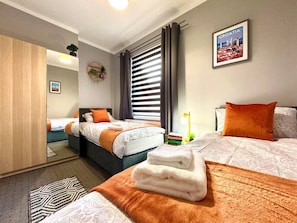 Een hotelkamer met twee bedden, een spiegel, een lijst met een afbeelding van Kroatië en een tafeltje met boeken en een lamp.