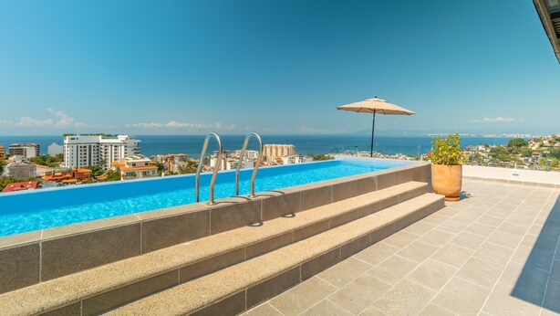Ein Pool auf dem Dach mit Stufen zum Wasser, einer Kübelpflanze und Blick auf Stadt und Meer.