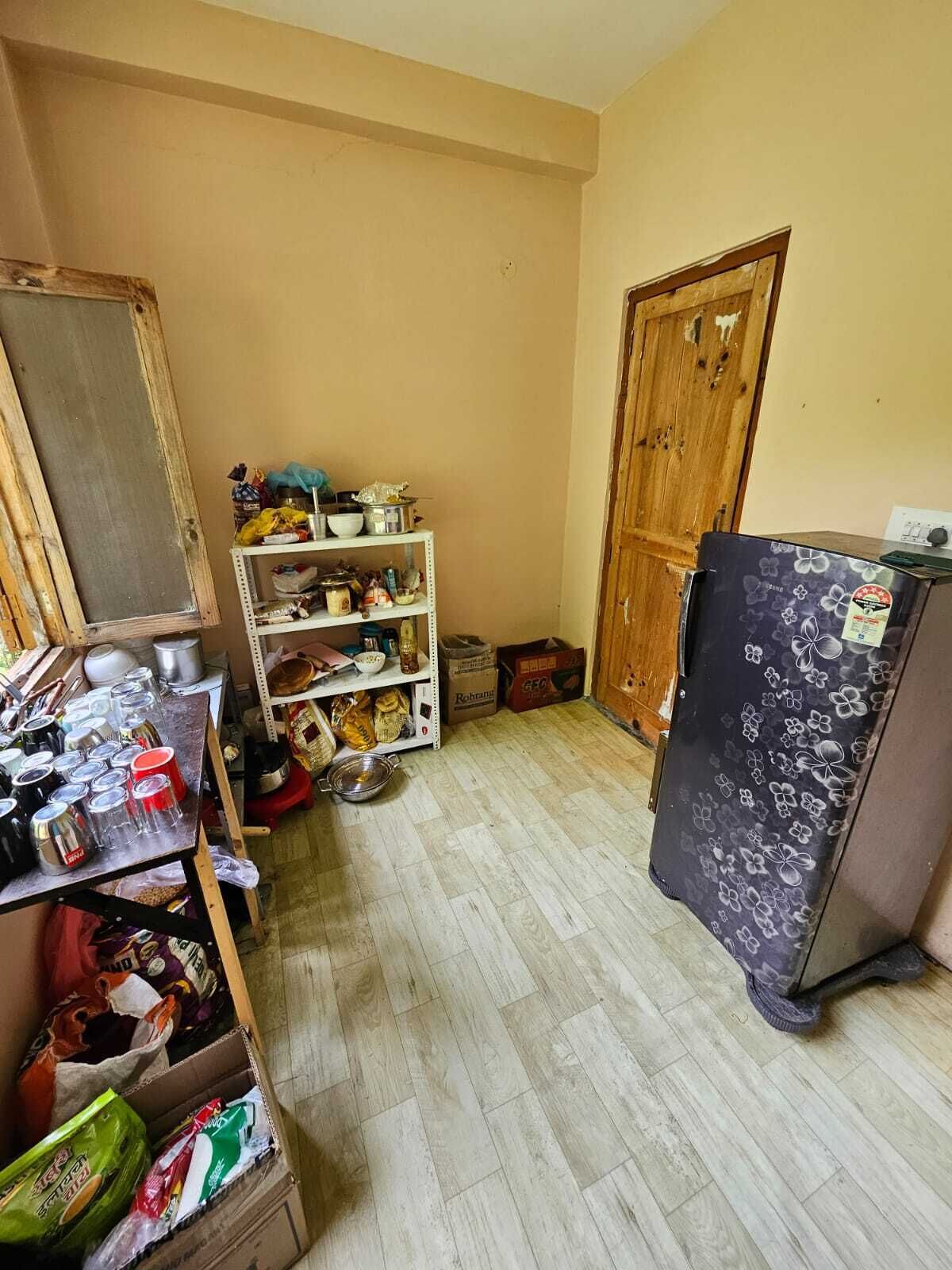 A compact kitchen with a refrigerator, shelves with various items, and a wooden door.