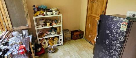 A compact kitchen with a refrigerator, shelves with various items, and a wooden door.