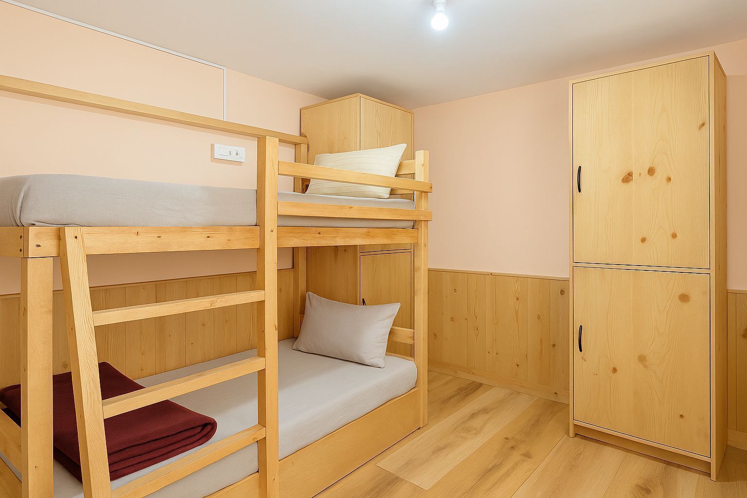 Een slaapkamer met een stapelbed, een garderobe en een lichtschakelaar op de muur.