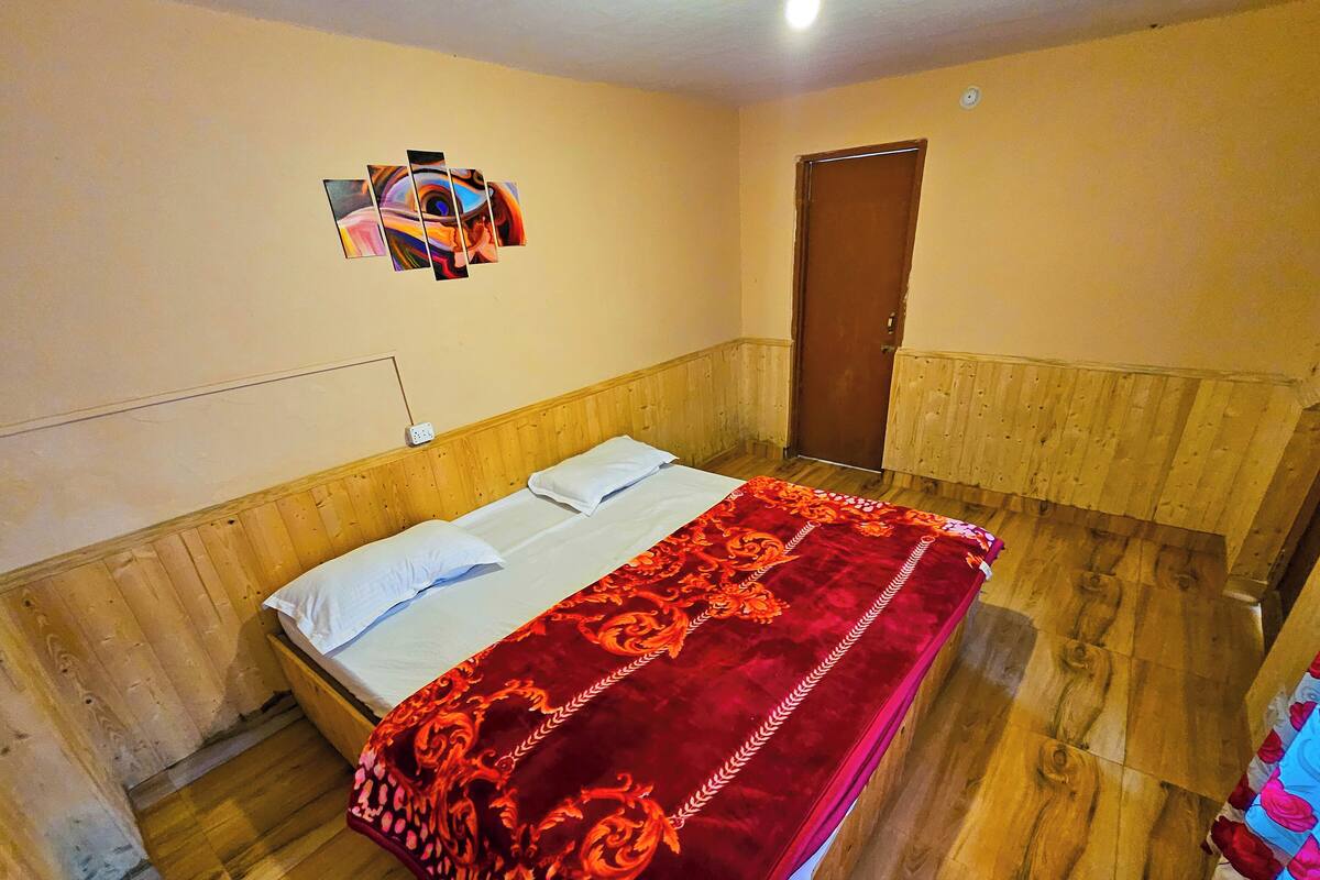 Une chambre avec un lit doté d’une tête de lit en bois, une couvre-lit rouge à motifs et une œuvre d’art accrochée au mur.