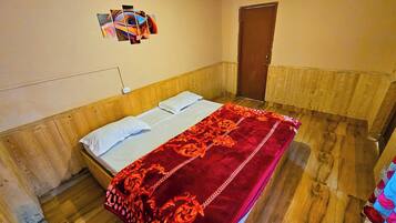 A room with a wooden headboard bed, a red patterned bedspread, and a wall-mounted artwork.
