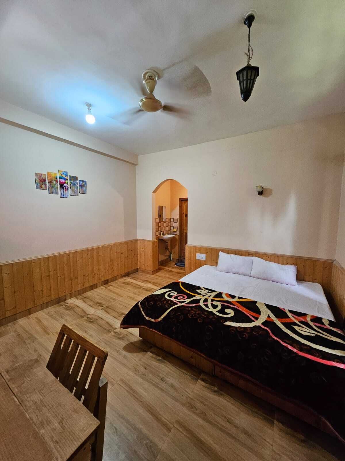 A room with a bed, a desk, and a ceiling fan. There is a small table and a chair in the corner.