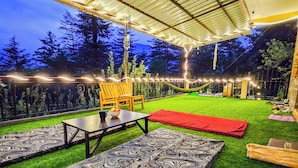 Un espace extérieur aménagé avec une terrasse, du gazon synthétique, une table, des chaises et un hamac.