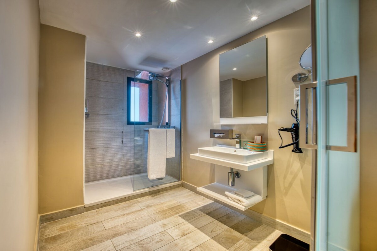 A modern bathroom with a glass shower enclosure, a large mirror, and a white sink.