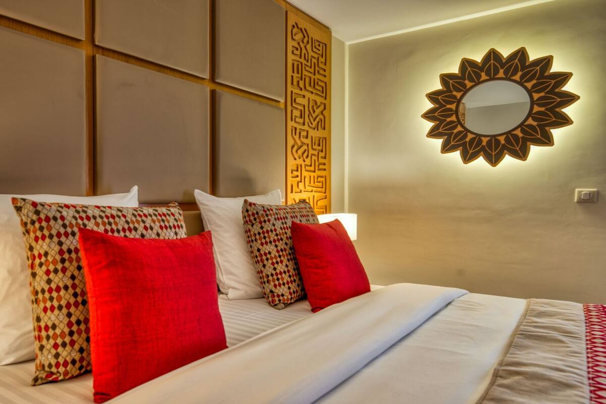 A hotel room with a bed, pillows, a wall-mounted mirror, and a decorative panel.