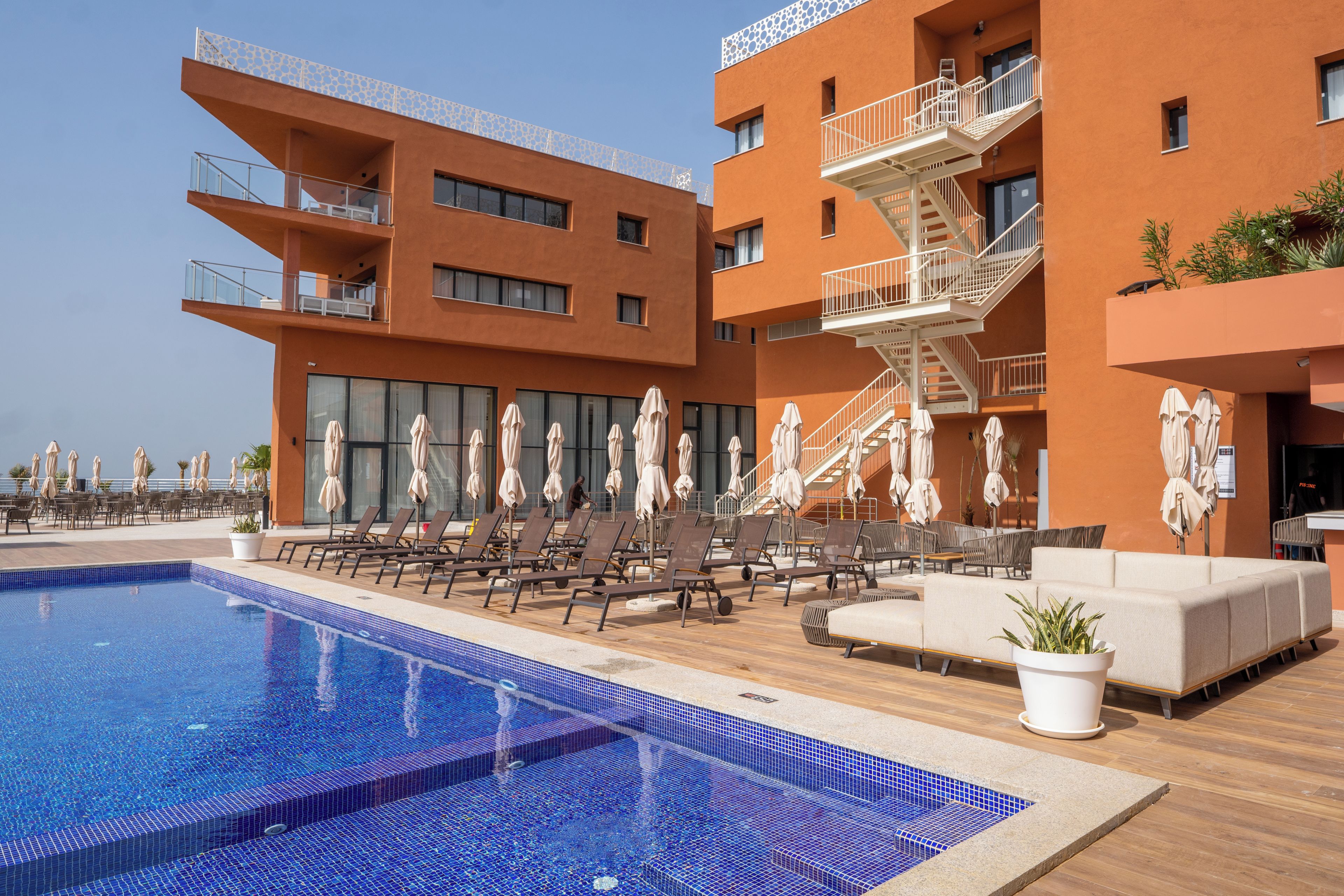 A modern hotel with a rooftop pool, sun loungers, and outdoor seating areas.