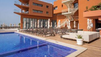 A modern hotel with a rooftop pool, sun loungers, and outdoor seating areas.