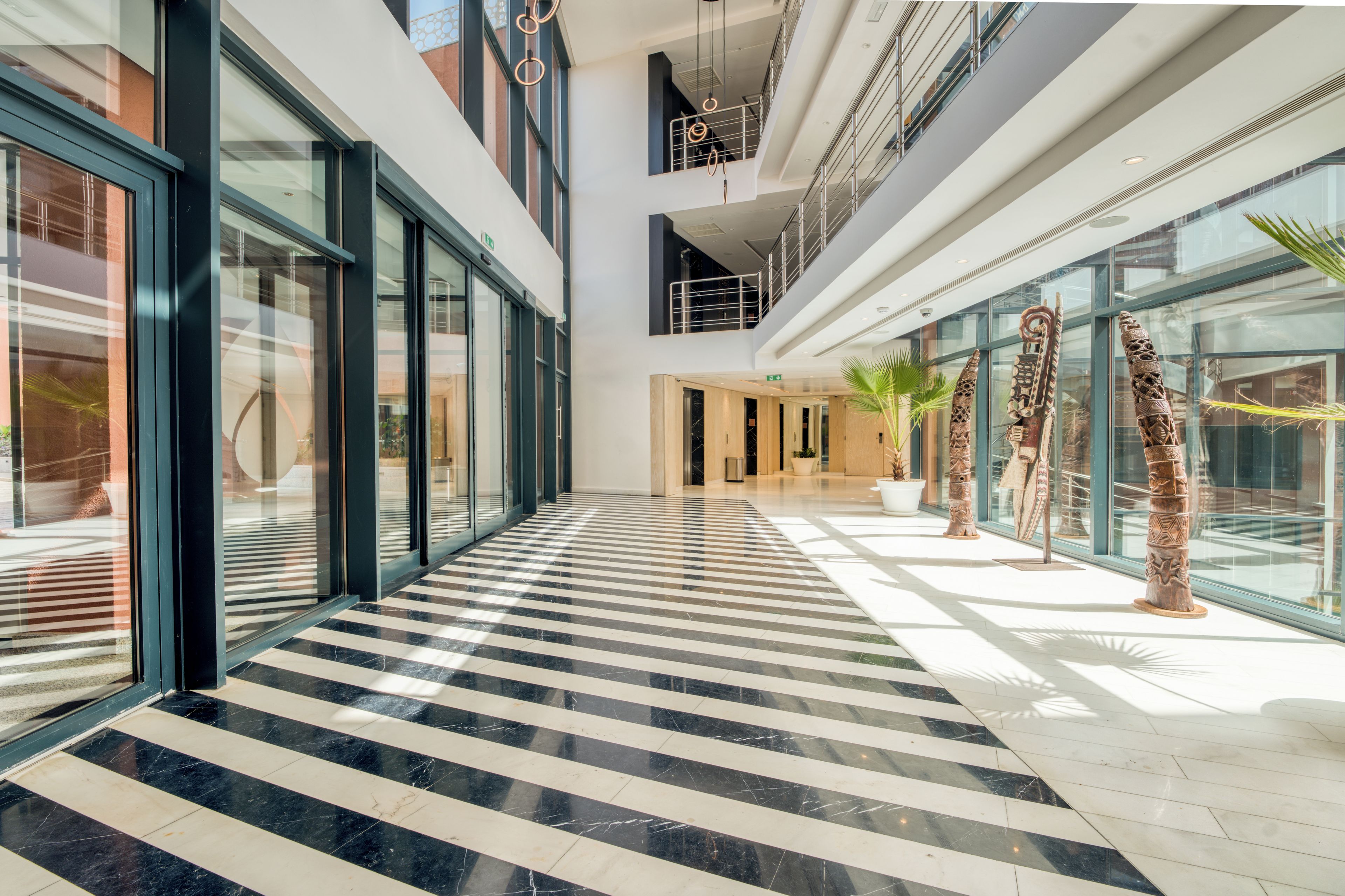 A modern hotel lobby with a checkered marble floor, large glass windows, and contemporary art sculptures.
