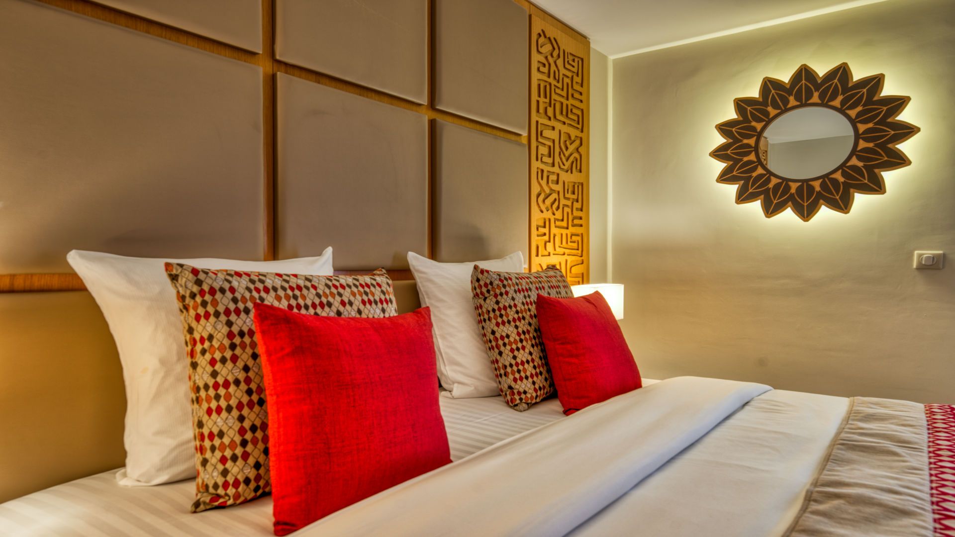 A hotel room with a bed, pillows, a wall-mounted mirror, and a decorative panel.