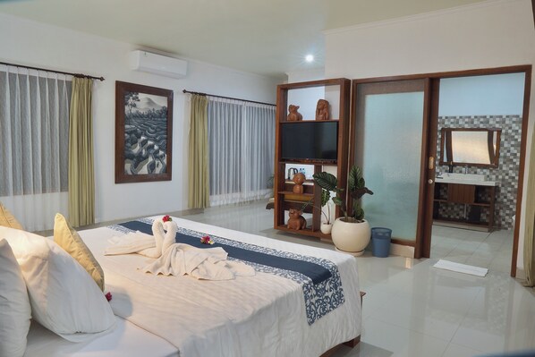 A hotel room with a large bed, a television, a bathroom with a mirror, and a sliding door leading to another room. - Giriya Amerta Hotel and Restaurant Ubud (Ubud)