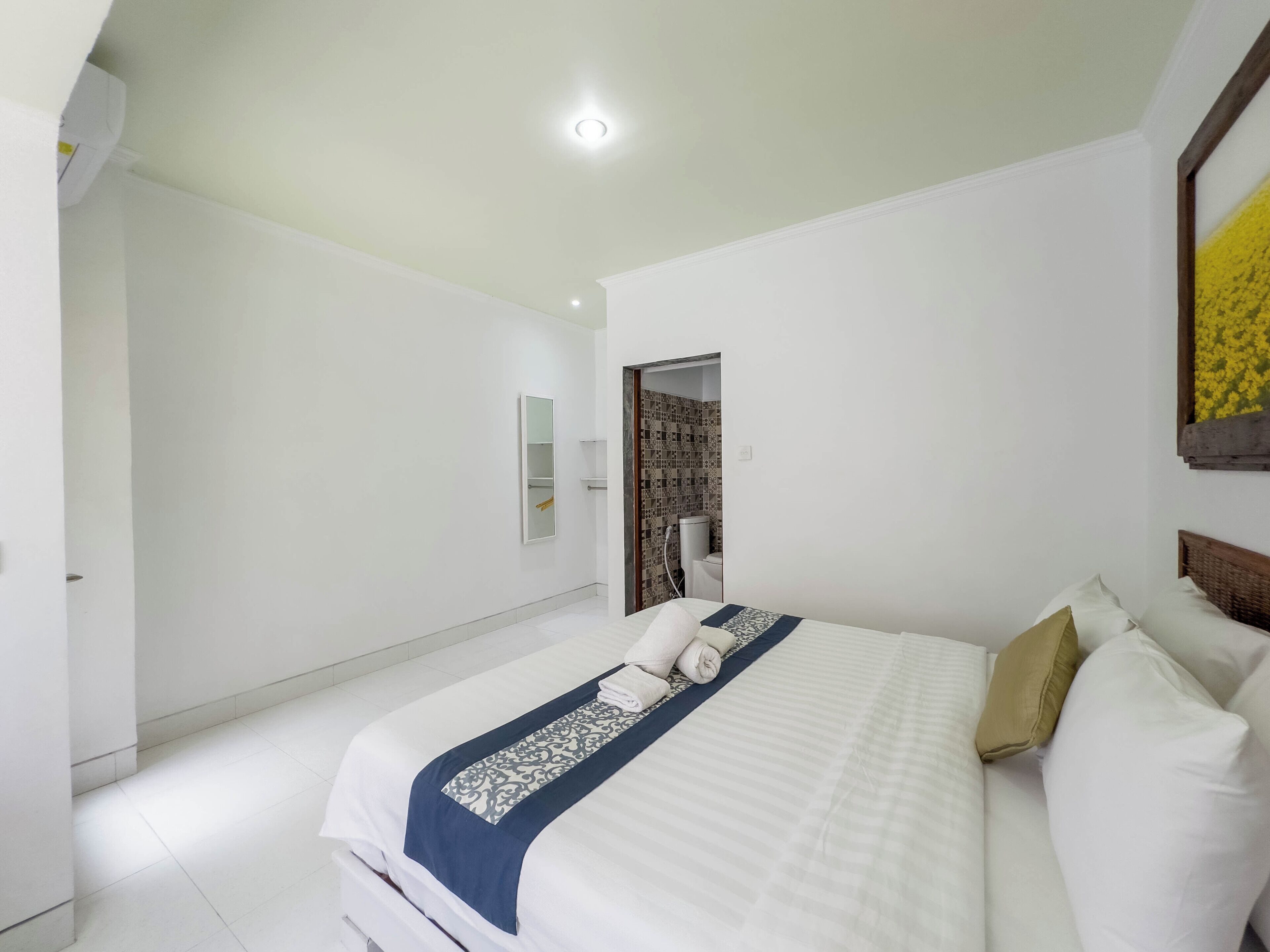 A hotel room with a neatly made bed, a bedside table, a mirror, and a view of the bathroom.