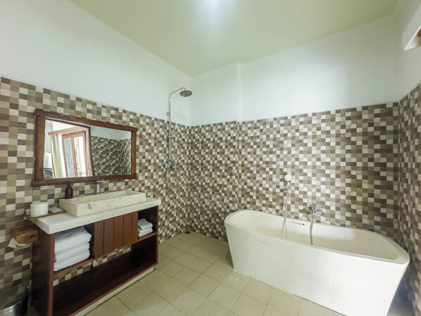 A bathroom with a checkered tile wall, a freestanding bathtub, a vanity with a mirror, and a shelf with towels. - Giriya Amerta Hotel and Restaurant Ubud (Ubud)