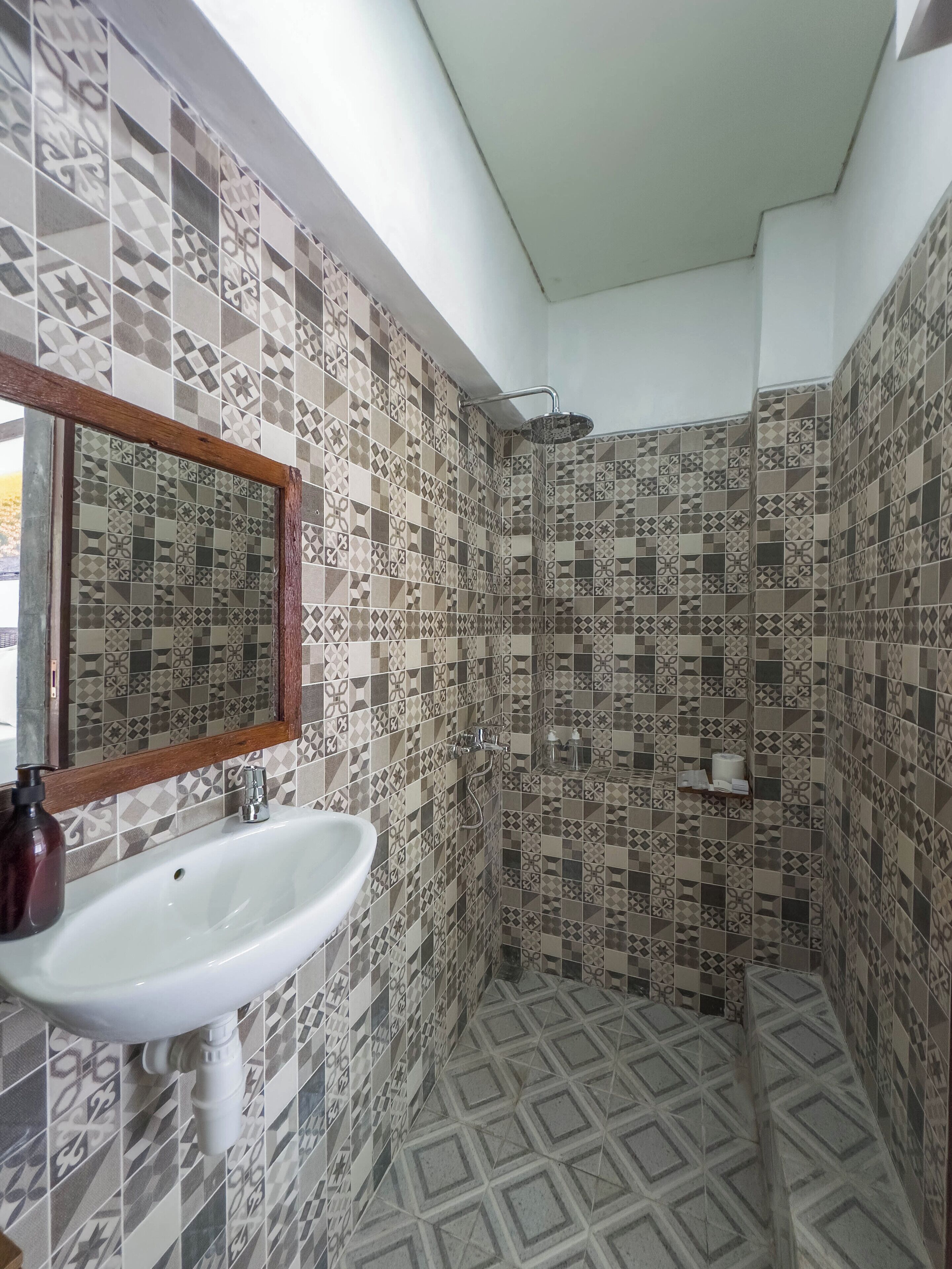 Un baño con lavamanos blanco, un espejo y una zona de ducha con azulejos estampados.