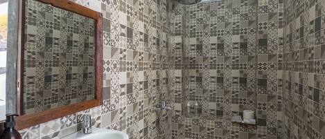 Un baño con lavamanos blanco, un espejo y una zona de ducha con azulejos estampados.