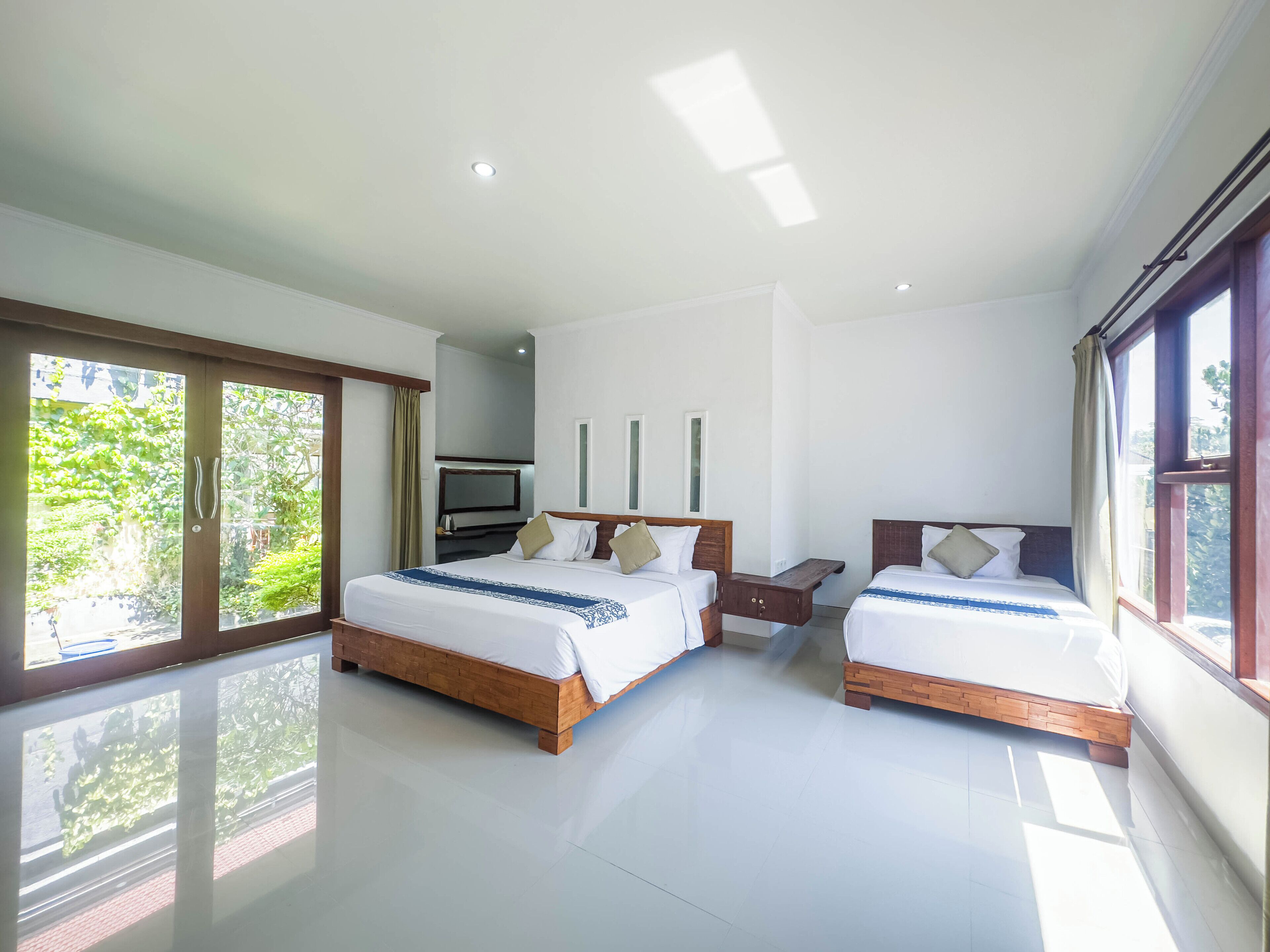A modern hotel room with two wooden beds, a flat-screen TV, and large windows offering a view of greenery.
