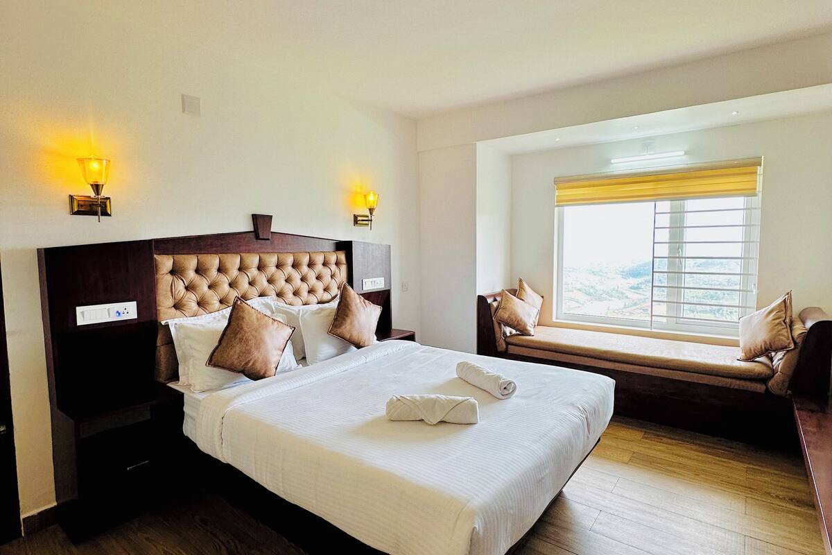 A hotel room with a large bed, a bench by the window, and two wall-mounted lamps.