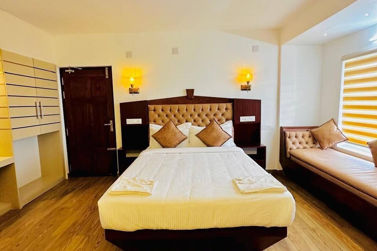 A bedroom with a large bed, wooden flooring, a sofa, and two bedside lamps.