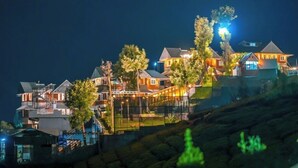 A hillside residential area with multiple houses, each with a distinct architectural style, featuring various roof types and surrounded by greenery. - Kanavu Valley View Resort (Coonoor)
