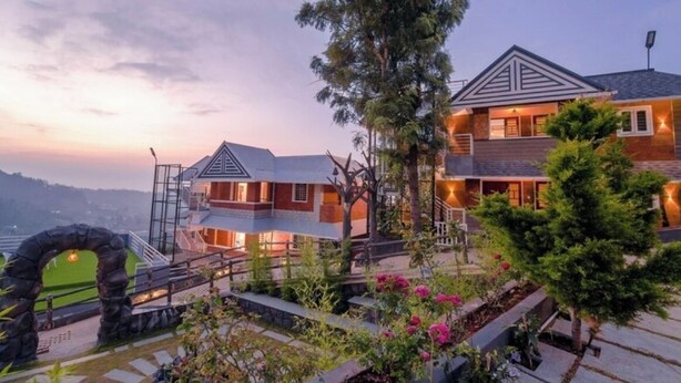 A modern two-story house with a stone archway entrance, surrounded by lush greenery and flowering plants. - Kanavu Valley View Resort (Coonoor)