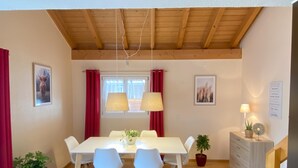 Een eethoek met een houten plafond, een witte tafel en blauwe stoelen.