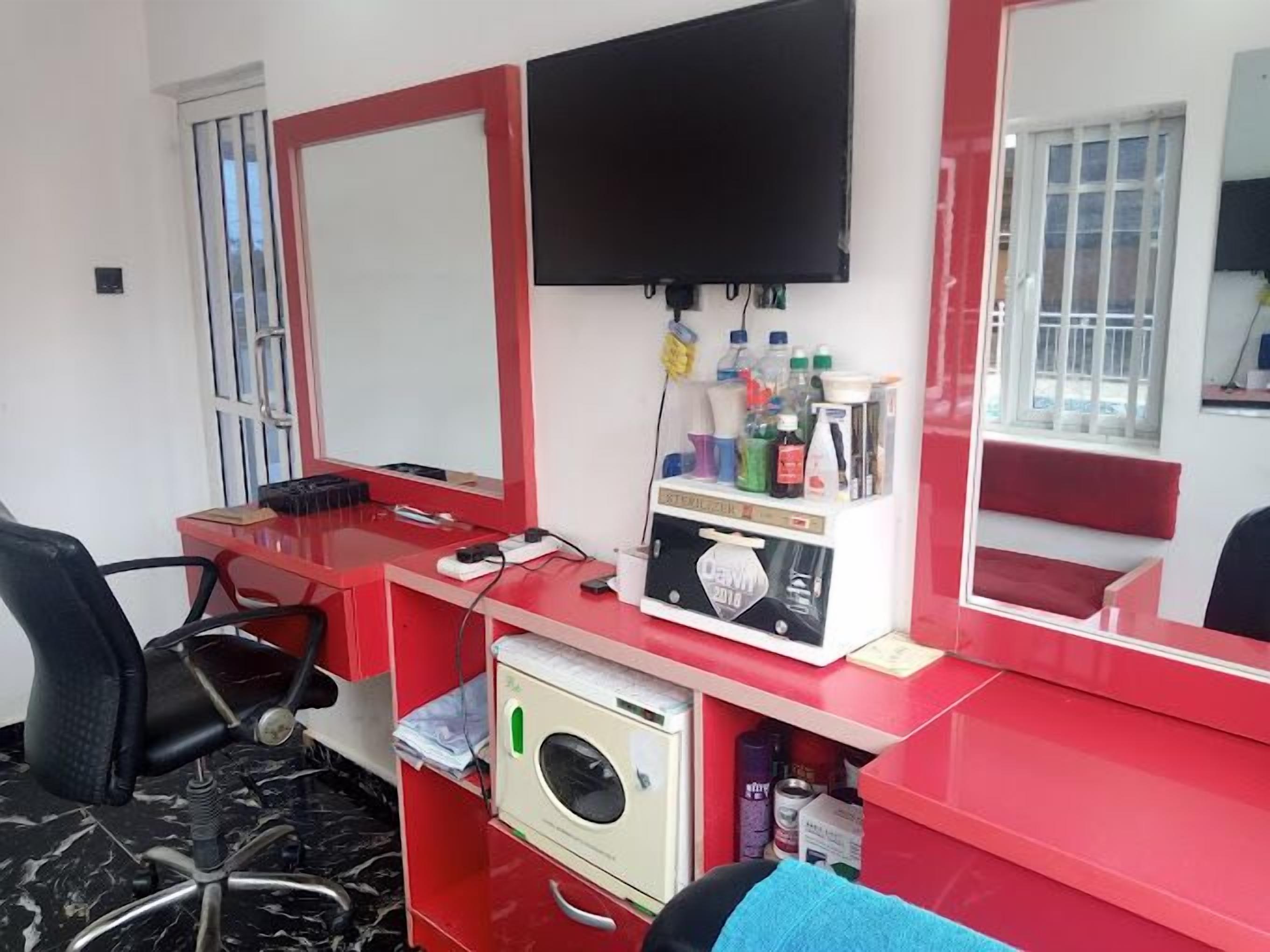 Ein Zimmer mit einem roten Schreibtisch, einem schwarzen Stuhl, einem an der Wand befestigten Fernseher und einem Spiegel.