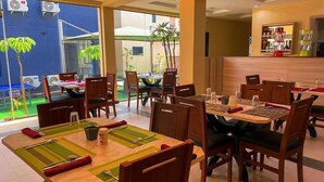 Un comedor con varias mesas y sillas, una zona de bar con diversas botellas y vistas al exterior a través de amplias ventanas.
