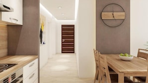 Una cocina moderna con armarios blancos, encimera de madera y estufa integrada. Hay un comedor con mesa y sillas de madera, y un reloj fijado a la pared.