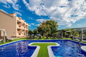 Ein Pool mit geometrischem Muster, umgeben von Liegestühlen und einem Gebäude mit Balkonen.