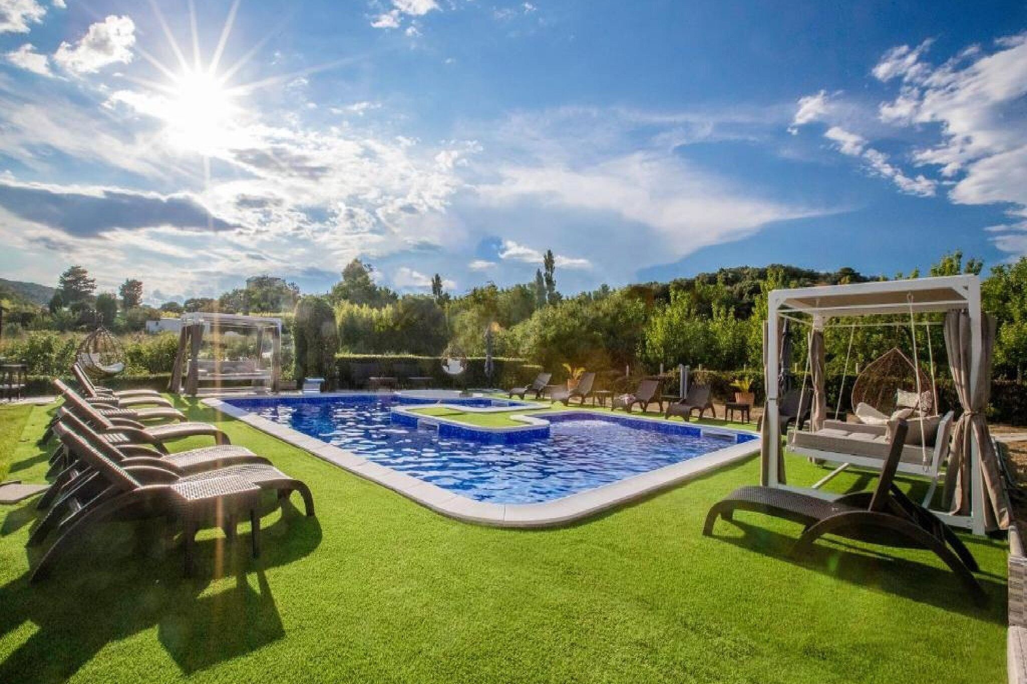 A swimming pool with a sunlit sky, surrounded by green artificial grass and lounge chairs.