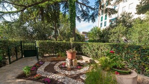 Un jardín ajardinado con un sendero de piedra, una jardinera central y vegetación circundante.