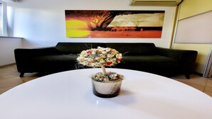 Una planta en maceta sobre una mesa blanca en una habitación con un sofá negro y un cuadro en la pared.