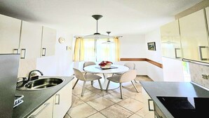 Una cocina compacta con una mesa redonda para comer, cuatro sillas, un lavamanos integrado y un ventilador de techo.
