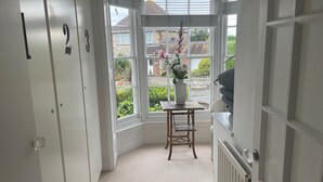 A corner room with a bay window, a white radiator, and a small wooden table with a vase of flowers. - Elm Cottage, first floor apartment with stunning coastal views (Seaview)