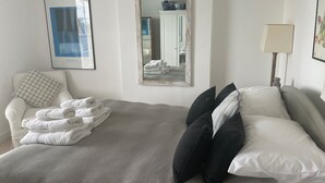 A neatly arranged bedroom with a bed, a chair, a lamp, and a mirror. - Elm Cottage, first floor apartment with stunning coastal views (Seaview)