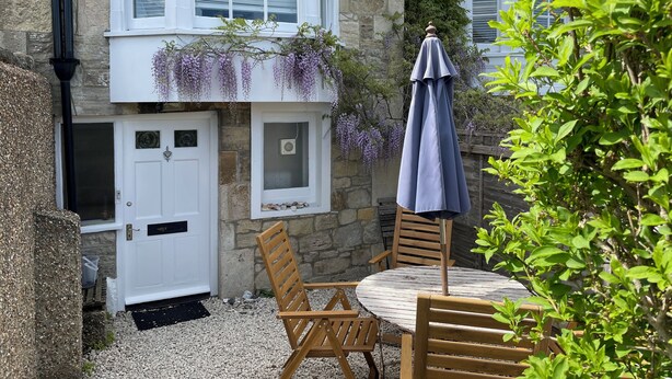 A stone building with a white door, a window with shutters, and a wooden table with chairs. - Elm Cottage, first floor apartment with stunning coastal views (Seaview)