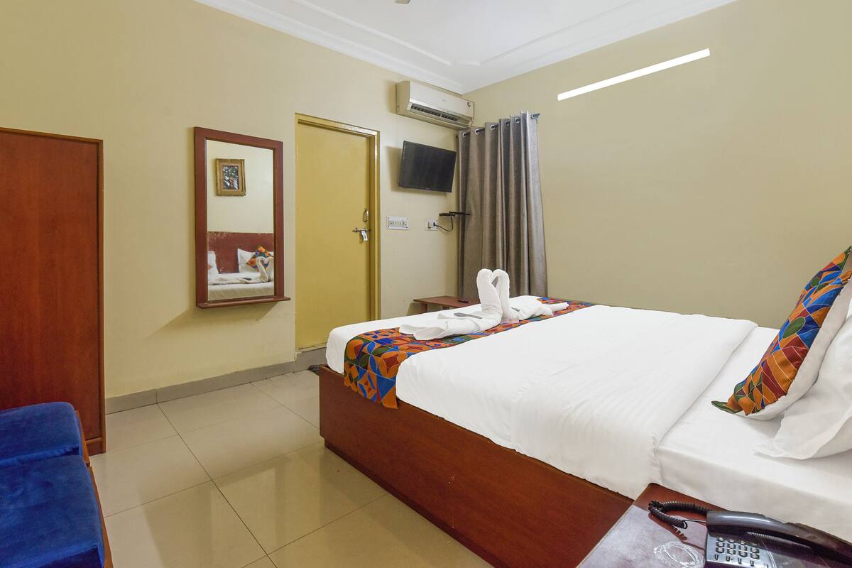 Une chambre d’hôtel équipée d’un lit, d’une chaise, d’un bureau avec un téléphone, d’un miroir, d’une télévision et d’un appareil de climatisation.