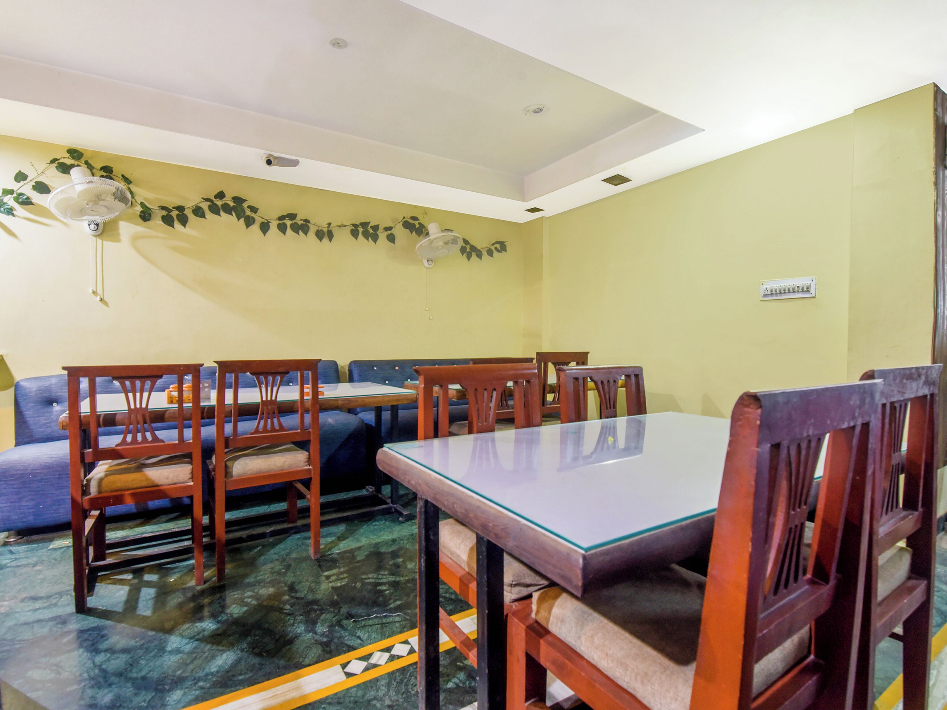 A dining area with a glass-top table, wooden chairs, a blue sofa, and a ceiling fan.