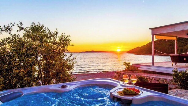 A hot tub with a sunset view, a table with a plate of food and a glass, and a covered seating area.